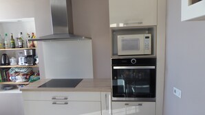 Une cuisine moderne équipée d’un four à micro-ondes, d’un four traditionnel et d’une plaque de cuisson intégrée. On y trouve des placards et un plan de travail sur lequel sont disposés divers objets.