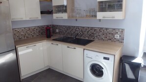 Une cuisine de taille réduite avec des meubles blancs, un lave-linge et un pare-feu en carrelage.