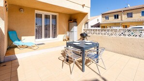 A patio with a table and chairs, a blue lounge chair, and a grill.