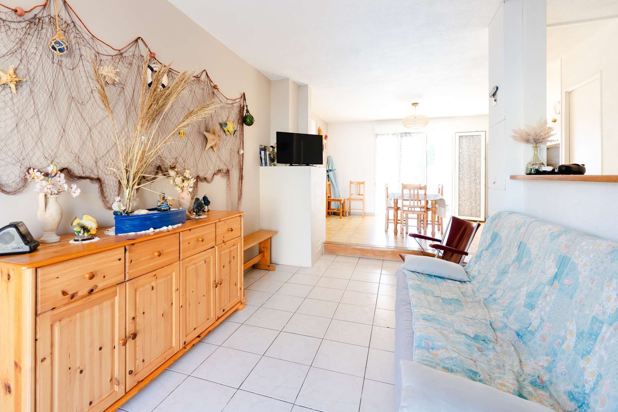 A spacious living area with a wooden cabinet, a blue sofa, and a television on the wall.