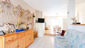 A spacious living area with a wooden cabinet, a blue sofa, and a television on the wall.