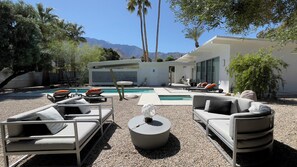 Un espace de vie extérieur moderne, doté d’une piscine, de coins salon et offrant une vue sur les montagnes.