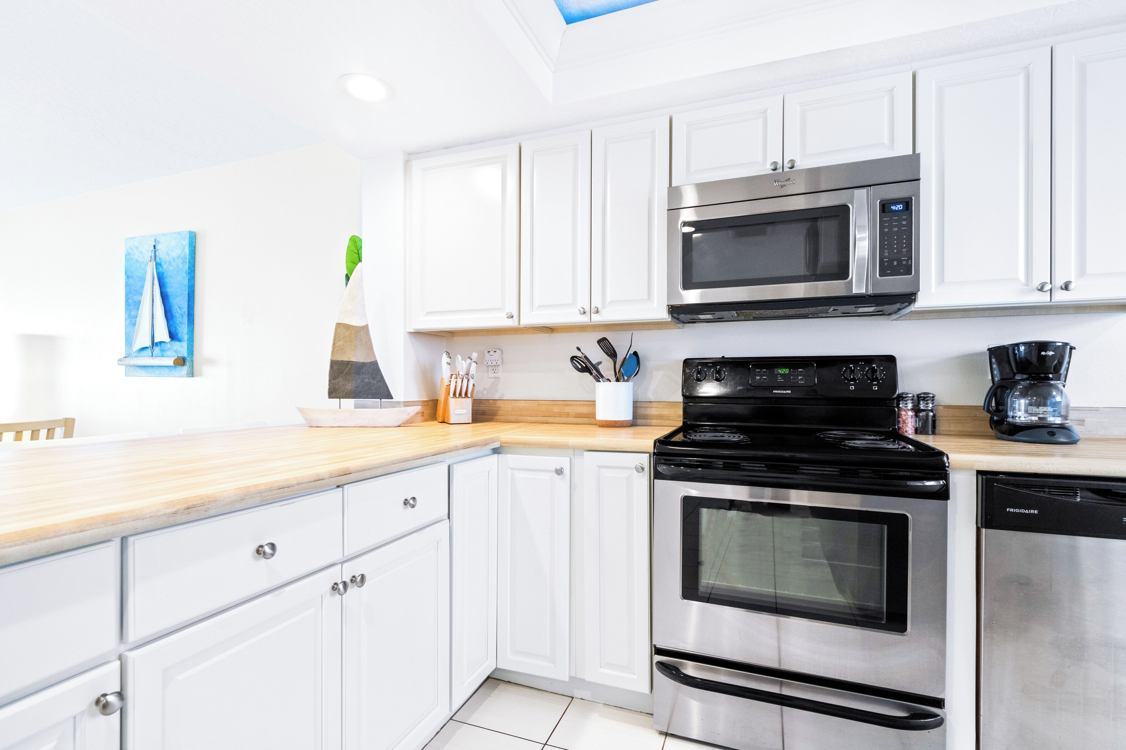 A modern kitchen with white cabinets, stainless steel appliances, and a wooden countertop.
