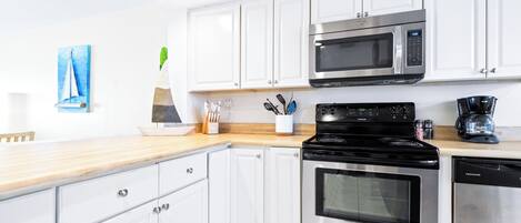 A modern kitchen with white cabinets, stainless steel appliances, and a wooden countertop.