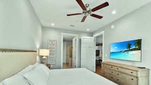 A bedroom with a bed, a ceiling fan, a TV on the wall, and a door leading to another room. - Moorings 104 Beautiful Marsh Front Condo (Jekyll Island)
