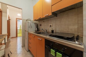 Een koelkast, een oven, een kookplaat, kookgerei, borden en bestek