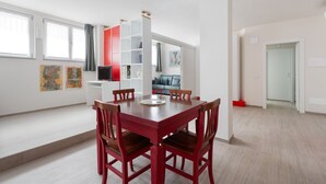 Een moderne eethoek met een rode tafel en stoelen, een witte kast en kunstwerken aan de muren.