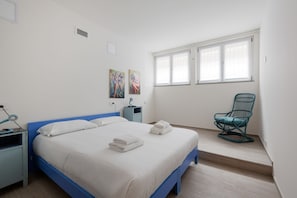 Un dormitorio con cama, una silla, una mesita de noche y una ventana.