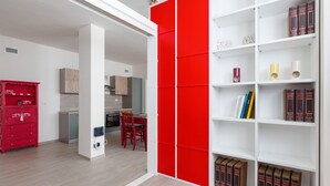 Een modern interieur met een rode scheidingswand, een witte boekenkast met boeken, een rode kast en een eethoek.