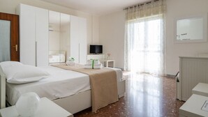 A hotel room with a bed, a TV, a desk, and a window with curtains. - GuestHost - Large and bright apartment that can accommodate up to 5 people with 2 bedrooms and 2 bathrooms, which boasts a beautiful view of the Villa di Sant'Antonio and, in the distance, of the sea from the balcony and window. Located a few steps from  (Monopoli)