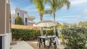 A patio with a table and chairs, a white umbrella, and palm trees.