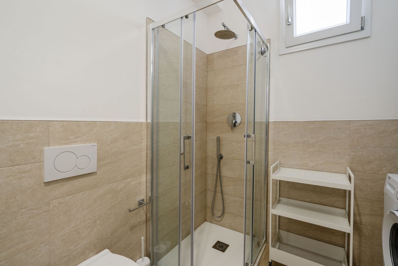 Eine begehbare Glasdusche mit Handbrause, einer fest montierten Bedienkonsole und einem weißen Ablagekorpus.