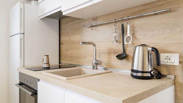 A modern kitchen with a built-in oven, a sink, a kettle, and a wooden backsplash.