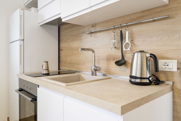 A modern kitchen with a built-in oven, a sink, a kettle, and a wooden backsplash.