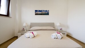 A hotel room with a bed, two bedside tables with lamps, a window, and a painting on the wall.