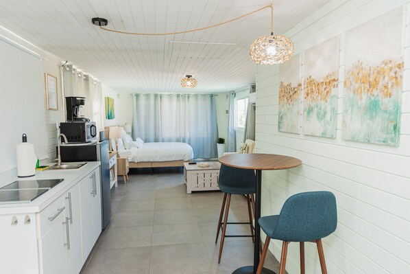 A modern, well-lit room with a kitchenette, a bed, a dining area, and artwork on the walls. - White Lotus Retreats (Noord)