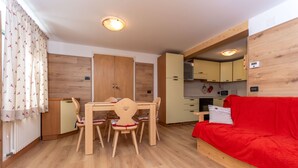 A compact living space with a dining area, kitchenette, and a red sofa. - Casa Caviola Centro (Falcade)