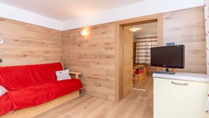 A room with a wooden wall, a red sofa, a television on a cabinet, and a wooden door leading to another room. - Casa Caviola Centro (Falcade)