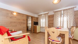 A room with a wooden floor, a bed with a red blanket, a wooden table with chairs, and a television in the corner. - Casa Caviola Centro (Falcade)