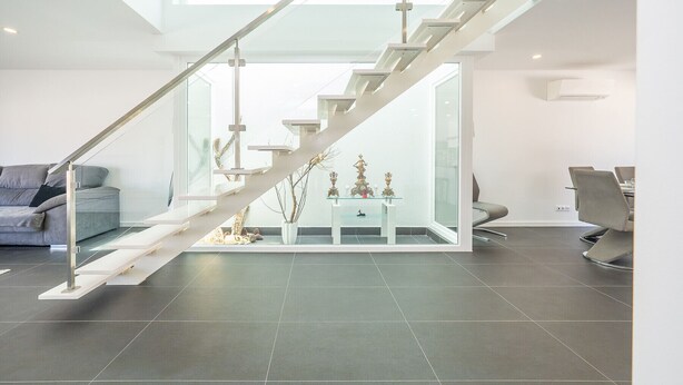 Een modern interieur met een glazen trap, een bank en een eethoek.