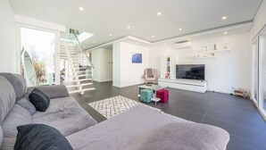 Een moderne woonkamer met een trap, een flatscreen televisie en een glazen deur naar buiten.