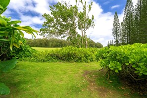 A well-maintained garden with a variety of plants and trees, a clear path, and a view of a distant field. - Kuilima Estates | Golf View 2 BR | Car Incl. w/ 6+ Nights | KUL-E113 by KBM (Kahuku)