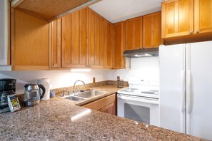 Une cuisine avec des meubles en bois, un plan de travail en granit, un évier en acier inoxydable, une cuisinière blanche et un réfrigérateur blanc.
