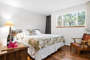 A hotel room with a bed, a nightstand with a bottle and glass, a chair, and a window with a view of trees.