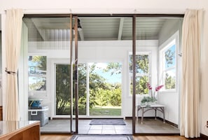 A room with a sliding glass door leading to a garden, a small table with a vase of flowers, and a blue mat at the entrance.