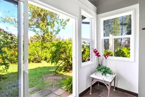 A conservatory with a glass door leading to a garden. Inside, there is a small table with a potted plant.