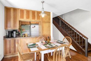 A kitchen with wooden cabinets, a white refrigerator, and a dining table set for four with chairs. - Kuilima Estates | Golf View 2 BR | Car Incl. w/ 6+ Nights | KUL-E113 by KBM (Kahuku)
