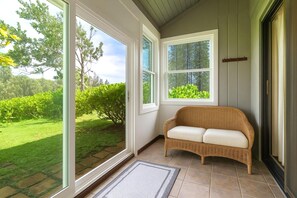 Quarto com um sofá de vime, janelas amplas e vista para um jardim.