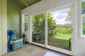 Una habitación con una puerta corrediza de vidrio que da a un jardín. Hay una silla azul y un enfriador gris en el suelo.