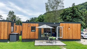 A modern, wooden cabin-style building with a patio area featuring a table and chairs, surrounded by a well-maintained lawn. - Villa Ramses by Interhome (Riedenburg)
