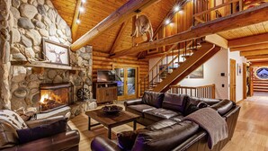 A log cabin interior with a stone fireplace, leather furniture, and a wooden staircase. - Bridger Lodge: Ski-In Ski-Out/Hike/Bike/Fish/Hunt Bridger Bowl Ski Area (Bozeman)