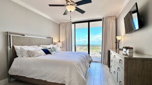A bedroom with a bed, a ceiling fan, a TV, and a view of the outdoors. - 2 FREE Beach Services ☀️Ocean View | Private Beach  Heated Pool | Gym | B-ball | Hot Tub (Miramar Beach)