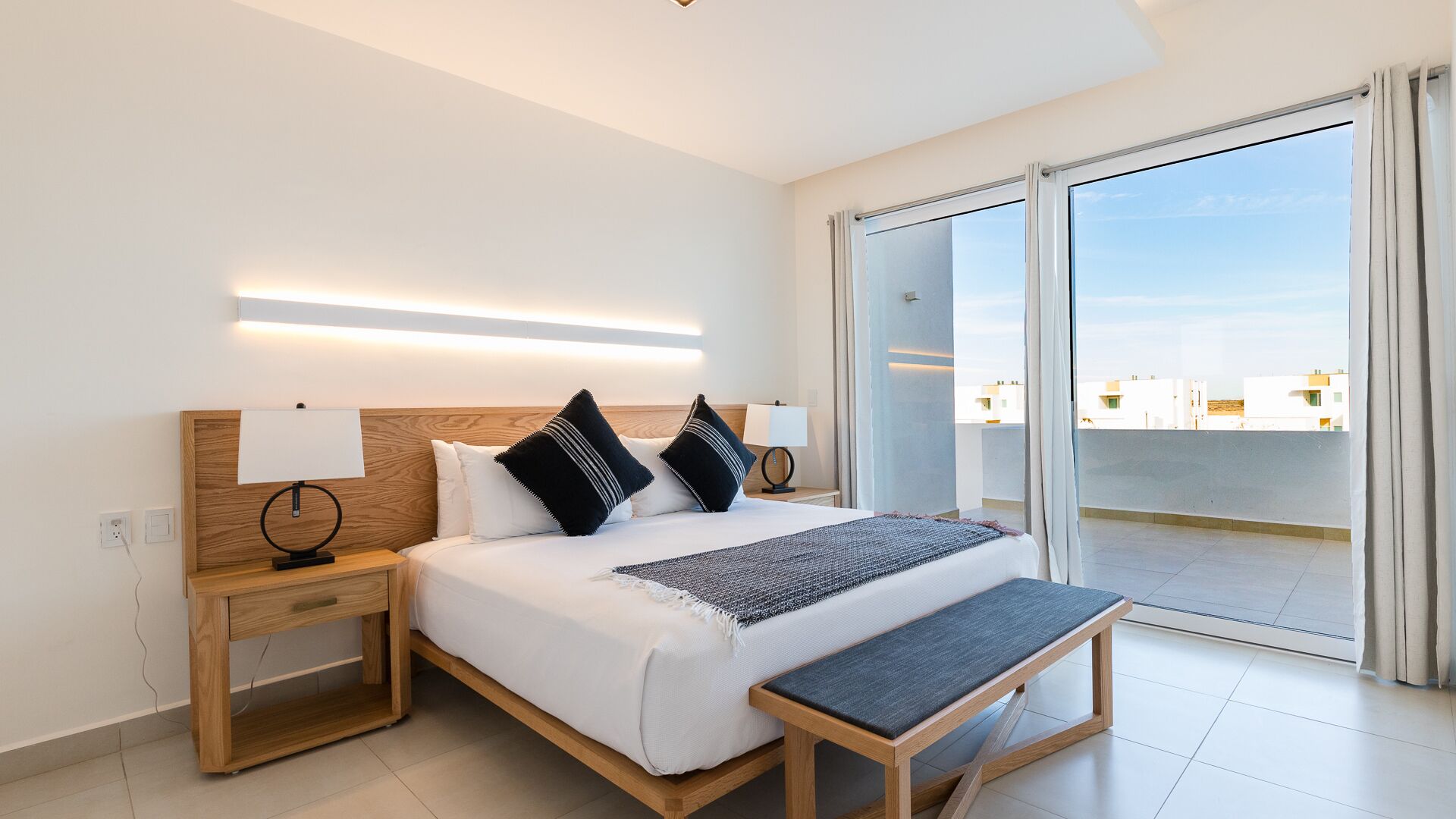 Ein modernes Hotelzimmer mit einem großen Bett, Nachttischen, einer Bank und einem Balkon mit Blick auf die Stadt.