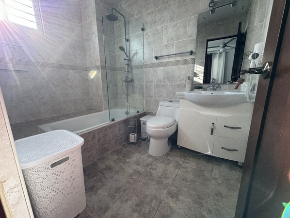 Un baño con ducha separada por vidrio, inodoro blanco y lavamanos con espejo arriba.
