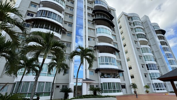A multi-story hotel with balconies, palm trees, and a paved entrance area.