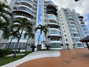 Un hotel de varios pisos con balcones, palmeras y un área de entrada pavimentada.