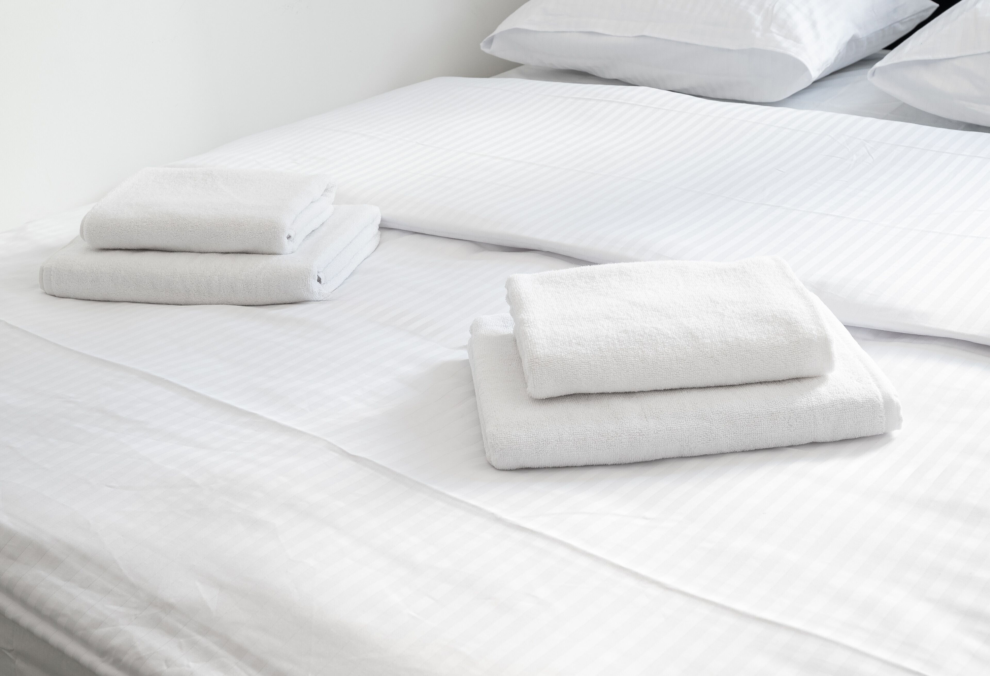 A neatly made bed with white linens and folded towels.