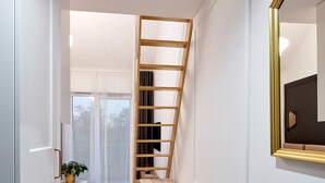 A narrow hallway with a wooden ladder, a small table, and a chair. - Nadolnik Apartment with Mezzanine (Poznan)