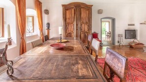 A spacious dining room with a long wooden table, ornate wooden doors, and a chandelier.