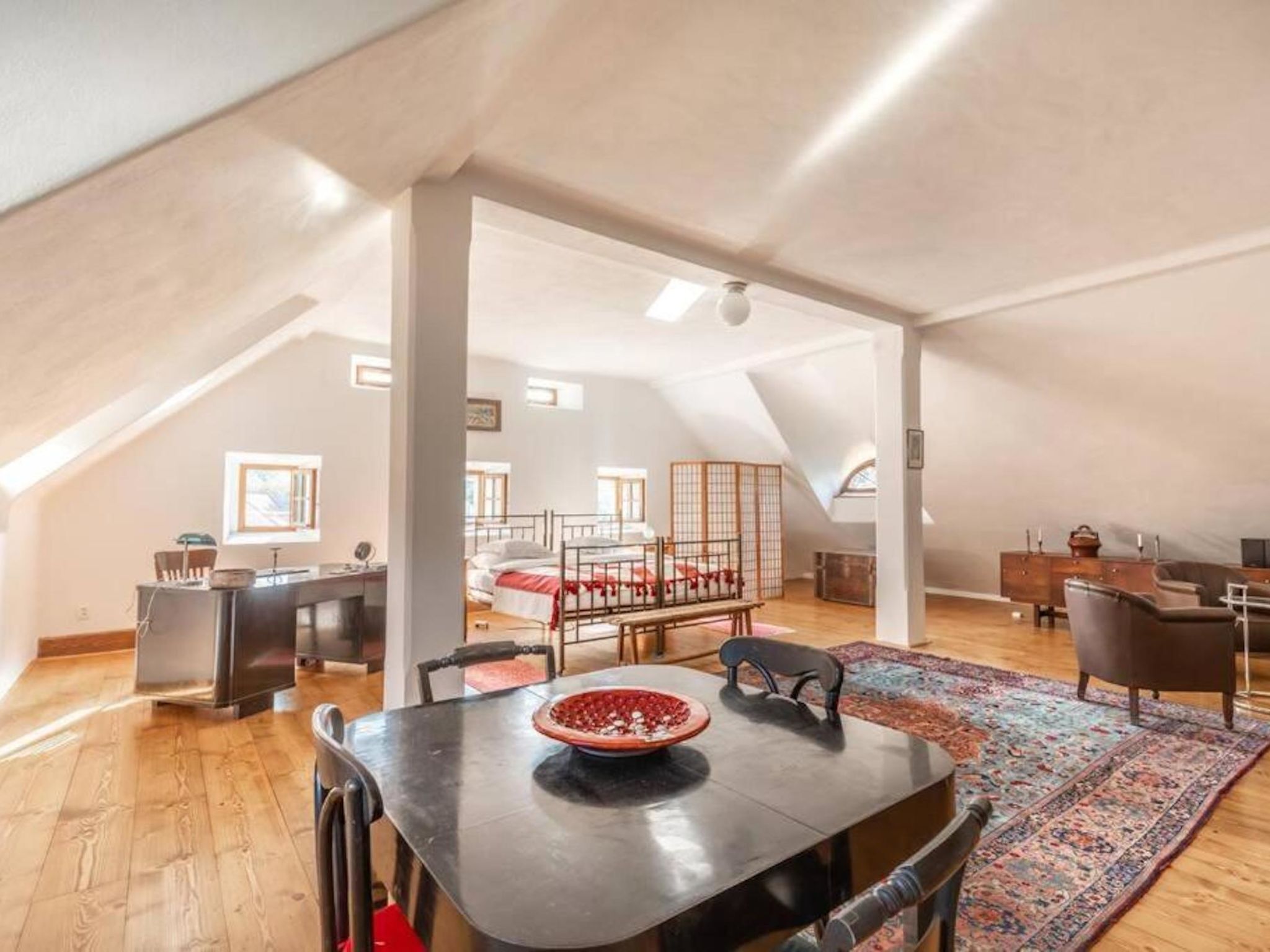 An attic bedroom with a dining area, a bed, and a desk.