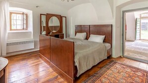 A bedroom with a wooden bed, a large mirror, a chandelier, and a view through an open door.