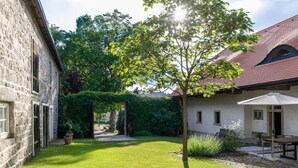 A stone building with a red-tiled roof, a well-maintained lawn, and a tree in the center.