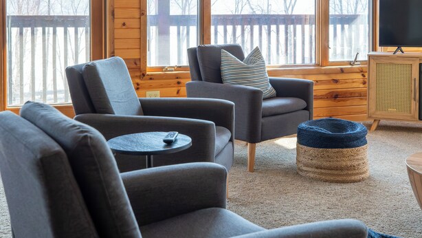 Una sala de estar acogedora con chimenea, asientos cómodos y grandes ventanales con vistas al exterior.