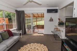 Relax in this open-plan living area with a comfortable sofa, TV, and bookshelf, leading to a patio with dining space.