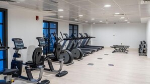Ein Fitnessraum mit mehreren Laufbändern und Ergometer, Holzboden und großen Fenstern.