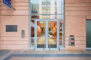 A hotel entrance with a glass door, a sign indicating the location, and a plaque with the name and address.